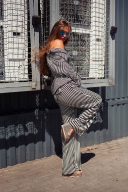 Pijamalı kız, bacağı krem arkaplanına yaslanmış vaziyette ayakta duruyor.