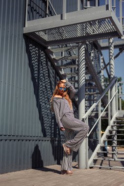 A girl in glasses and a loose suit straightens her hair and raises one leg. Full length photo of a girl.