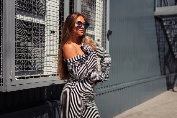 Açık renk elbiseli koyu tenli bir kız şehirde endüstriyel klimaların önünde poz veriyor.