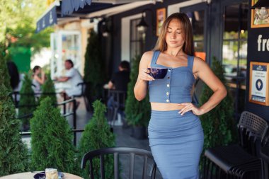 Ciddi bir kız selvi çiçekleri arasında bir kafede elinde bir bardak tutuyor. Serbest Çalışan Konsepti.