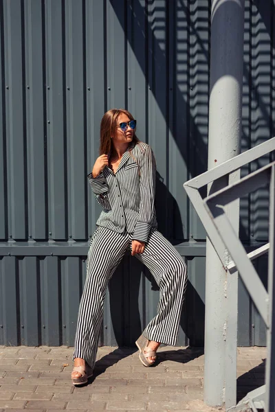 Kafkasyalı kız güneş altında gözlüklü ve çizgili bir takım elbiseyle öylesine oturuyor. Şehir tarzı. Madam başka tarafa bakıyor..