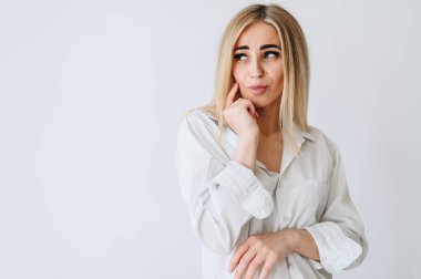A fair-haired girl with dark eyebrows looks away. Girl on a white background in a white shirt. The girl has a toothache.