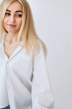 Portrait of a blonde woman who looks down to the side in a white shirt on a white background. Copy space in the right corner.