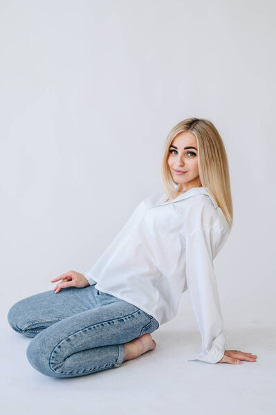 A girl in jeans and a white shirt leaned on her arm from behind. Girl on a white background in jeans.