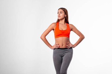 Turuncu spor bluzlu bir kız çerçevenin sağında duruyor, elleri kalçasında ve sola bakıyor. Beyaz siklonamada antrenör. Boşluğu kopyala.