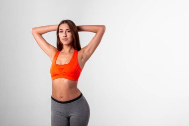 Parlak spor tişörtlü, elleri başının arkasında beyaz bir arka planda olan bir kız. Spor kulübü konsepti.