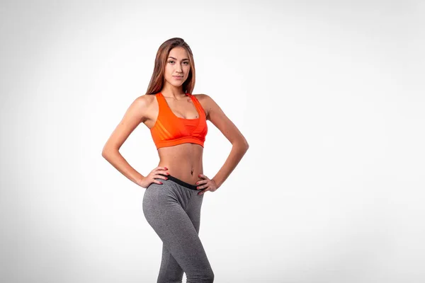 Spor kıyafetli bir kız beyaz bir arka planda yan duruyor.
