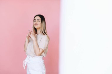 Bir kız ayakta dikiliyor ve pembe arka planda kameraya bakıyor, yarım beyaz arka planda. Zaman oluşturma kavramı.