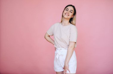 Hafif iplikleri ve hafif kıyafetleri olan bir kız neşeyle gülümser ve pembe bir arka planda özgürce durur..