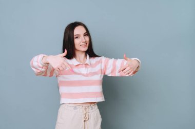 Bir öğrenci, çizgili süveter giyen neşeli, yaramaz bir kız, parmaklarıyla düz bir duvarı işaret ediyor..