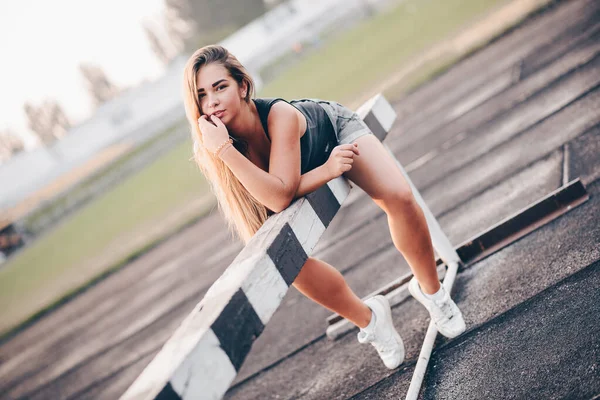 Dişi koşucu sabah antrenmanı sırasında dinlenmek için uzandı. Stadyumda ıslak asfalt ve yeşil çimenler.