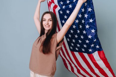 Bağımsızlık Günü 'nde özgürlüğünü kutlayan özgür melez hippi kız. Elinde Amerikan bayrağı sallayan mavi bir duvara yaslanmış kız.