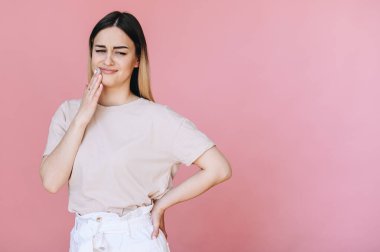 Pembe arka planda düz saçlı beyaz bir kadın diş ağrısı ya da diş ağrısı yüzünden yüzünde acı veren bir ifadeyle ağzına dokunuyor..