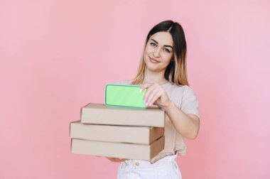 Telefonun yeşil ekranı. Pembe arka plandaki bir kızın elindeki kutuların üstündeki telefon. Hızlı online pizza teslimatı konsepti.