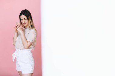 Bir kız ayakta dikiliyor ve pembe arka planda kameraya bakıyor, yarım beyaz arka planda. Metin için yer