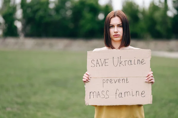 A girl with a sad face asks the world for help to save Ukraine. Young girl in nature with a sign in her hands to stop mass famine