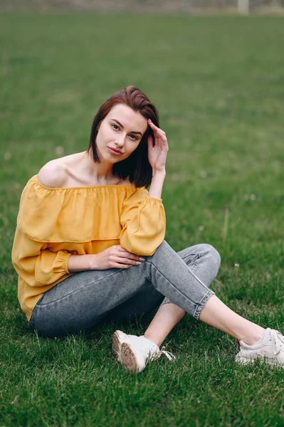 Dziewczyna Siedzi Zielonej Trawie Prostuje Włosy Skróconą Fryzurą Żółta Bluzka — Zdjęcie stockowe