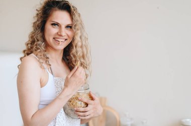 Kavanozdan çiğ makarna yiyen önlüklü, kıvırcık sarışın bir kadının yatay yakın plan portresi. Uzayı kopyala Aç kız konsepti