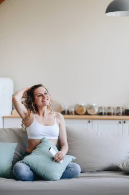Kanepede oturan genç bir kadının dikey fotoğrafı. Ev kıyafetleri içinde ve elleri kapalı, tatmin edici bir şekilde saçını düzeltiyor. Tatil kavramı