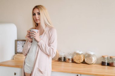 Mutfakta İki Elle Kupa Tutan Bir Kızın Portresi Ev Giysileriyle Gün Işığı Altında. Mutfakta parlak bir iç mekanda bir kız. Kahvaltı.