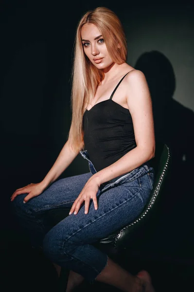 若い女性のスタジオの肖像画は 椅子に座って ゴボマスク効果と ジーンズと黒のTシャツ ゴールドの髪の垂直女の子 — ストック写真