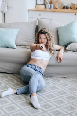 Dikey fotoğraf. Kız yerde oturuyor ve konsolun önünde duruyor. Basın mensubu kız gardırop bagajında oturuyor. Ev samimi iç mekan..