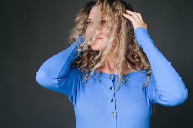 Mutlu gülümseyen kadın kafasını karanlık bir arka planda farklı yönlere çeviriyor. Kıvırcık saçlı mavi kazaklı bir kız. Yaşam tarzı kavramı.