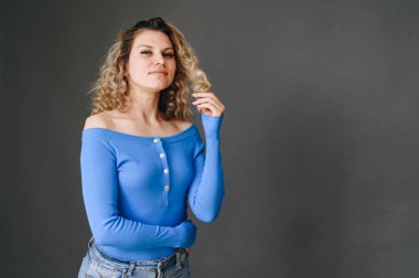 Gri arka planda düğmeleri olan parlak mavi ceketli mutlu bir kadın. Kopya alanı. Makyajsız kıvırcık kızın üstünde