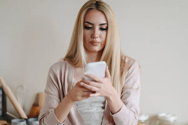 Sinirli, Öfkeli Sarışın Kadın telefonu elinde tutuyor. Dişi mutfakta duruyor ve telefonuna büyük bir portre çiziyor. Boş boşluk.