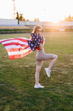 Sunset 'te Amerikan Bayrağı olan bir kızın dikey fotoğrafı. Bayrak Rüzgarda Gelişiyor. Bağımsızlık Günü Kavramı