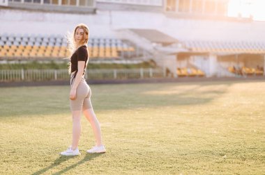 Stadyumdaki Slim Atletizm Kızı 'nın yatay fotoğrafı Spor Giyim' de Green Lawn 'da duruyor. Uzayı kopyala Stadyumda günbatımı.