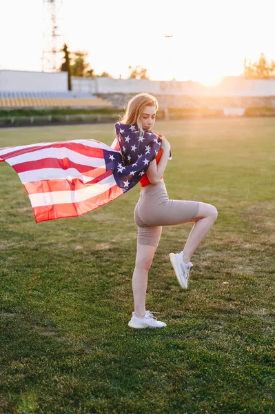 Vertical Photo of Girl with an American Flag at Sunset. Flag is Developing in Wind. Independence Day Concept