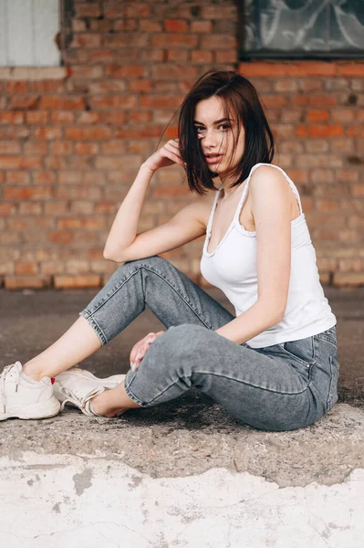 Young Positive Joyful Girl Jeans Sneakers Sits Smiles Concrete City — Stock Photo, Image