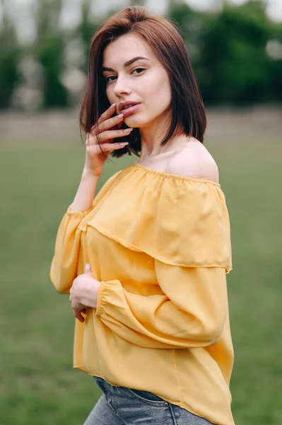 Young Woman in Yellow Blouse is Standing on Natural Background. Hand to lips. Beauty and skin care concept