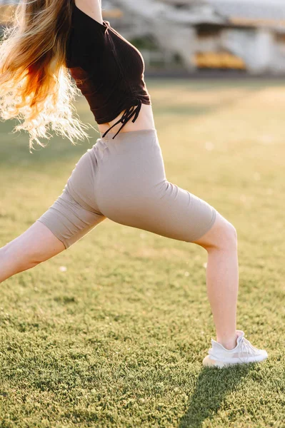 Athletic Girl Lunges Forward In The Sunbeams. Athletic buttocks in leggings Close-up. Part of Exercise in Nature on a Summer Day