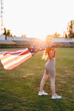 Genç bir kadın elinde bir Amerikan Bayrağı ile caddede duruyor. Bayrak rüzgarda dalgalanıyor. Spor Giyim Stadyumu 'ndaki kız. Amerikan Takımını Destekleyin.