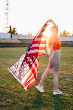 Stadyumdaki Kız Ayakta Duruyor ve Amerikan Bayrağı Tutuyor. Gün batımında bayrağı olan siluet kız. Stadyumda Atletik Zayıf Genç Sporcu