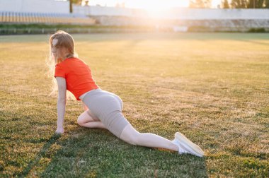 Kırmızı bluzlu atletik kadın bir bacağını uzattı ve esneme hareketleri yapıyor. Bir Yaz Akşamında Doğadaki Spor programına katılın. Sağlıklı bir hayat sür..