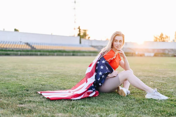 Cute Blonde Woman Sits Wrapped American Flag Green Lawn Стадіоні — стокове фото