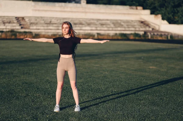 体育与健康主题 年轻美丽的白人女子在体育场进行热身运动 热身肌肉 夏天在人造草皮上种植绿色的腹部草 — 图库照片