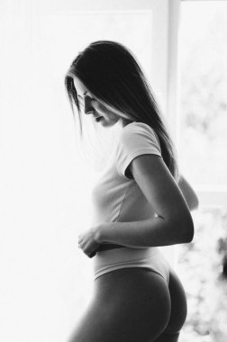 Beyaz külotlu seksi bir kızın siyah beyaz portresi pencereye karşı. Gürültülü Grainy fotoğrafı. Yıllanmış bir fotoğraf. Vücut bakımı kavramı.