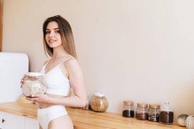 Güzel kadın vücudu. Bir kadın vücuduna iyi bakar ve sağlıklı beslenir. Mutfakta dikilirken elinde bir kavanoz yulaf ezmesi tutan genç bir kadın. Boşluğu kopyala.