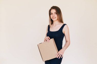 Bej arka planda elinde karton kutusuyla siyah elbiseli hoş bir genç kadın. Uzayı kopyala Doğal Görünümlü Kız Terfi Teslimatı