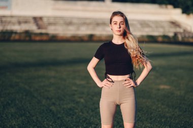 Genç Kadın Hiplerin Üzerinde Düz Ellerle Ayakta Duruyor. Stadyumdaki Yeşil Çimlerde Spor Giyimli Kız. Doğadaki Tatmin Edilmiş Atletik Kadın.