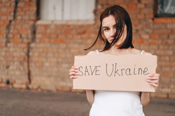 Women with Poster Save Ukraine. A woman with a belligerent look looks into the Camera. Wind develops Hair.