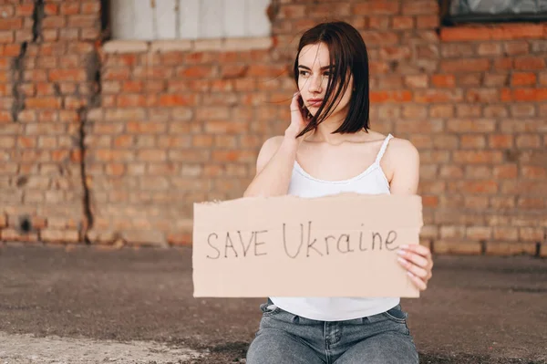 Women with Poster Save Ukraine. A woman with a belligerent look looks to the side. Wind develops Hair.