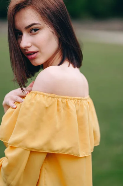 A Young Woman Stands Sideways in a Yellow Blouse. Hair covers half of the face. Soft blurred background. Advertising Cosmetics. Facial Skin Care