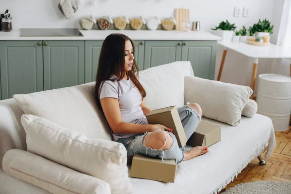 young woman in torn jeans sits pensively on sofa. girl is holding boxes in her hands. Concept Unemployed. Home cozy interior.