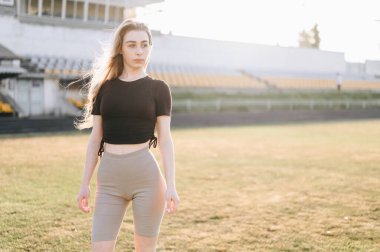 Sağlıklı aktivite. Sportif Siyah Üstlü Sarışın Kadın ve Bisiklet Şortlu Stadyumda Duruyor ve Tarafa Bakıyor. Spor Yaşam Tarzı Konsepti, Boş Alan