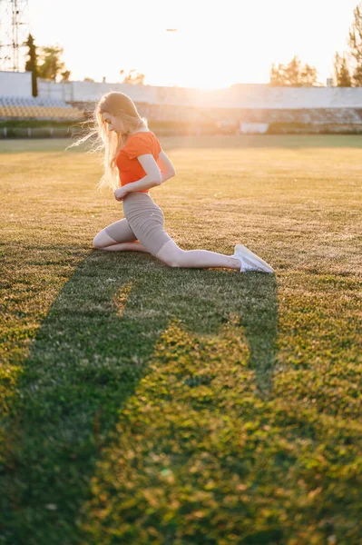 穿着运动服的年轻女子在草地上做伸展运动 女孩在晚上锻炼 前夜之光中的女孩夏天的黄金时光阳光下金丝雀中的运动员 — 图库照片